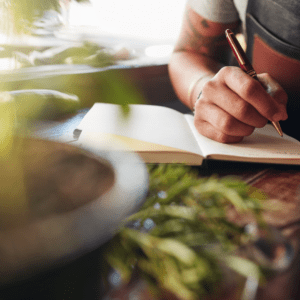 food is in foreground as male writer is describing the food with pen and paper